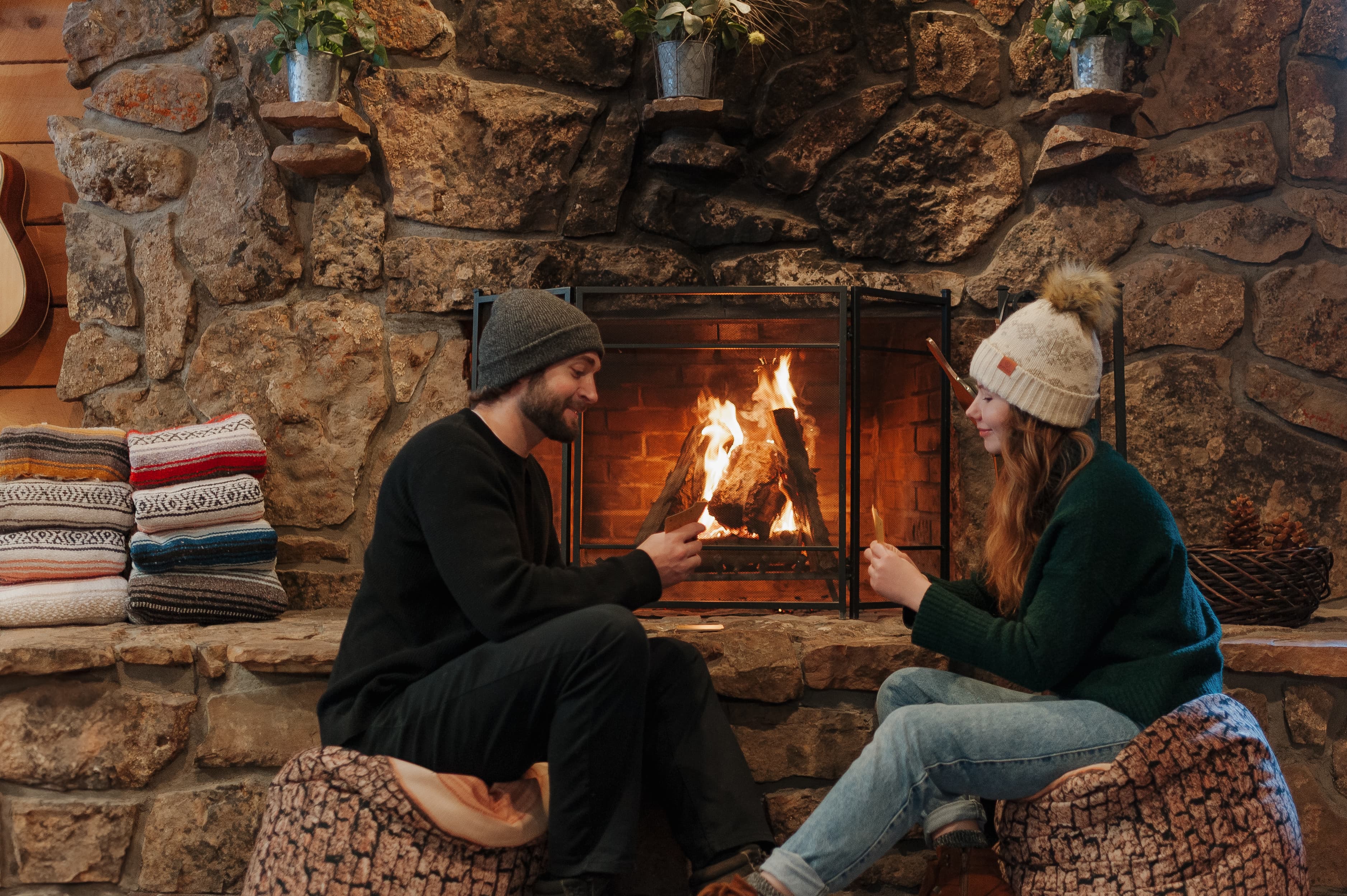 A cozy scene of a couple sitting by a stone fireplace, enjoying hot drinks in a rustic setting.