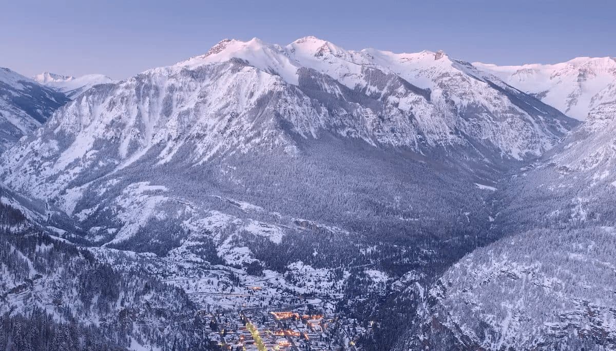 Snow-covered mountains towering over a small village at sunset.
