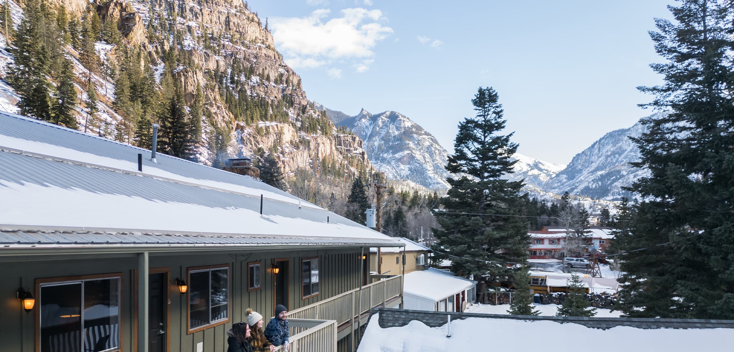 A cozy building in a snowy landscape surrounded by mountains and pine trees.