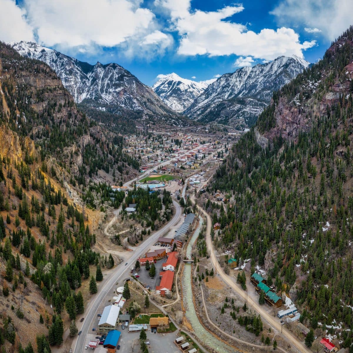 Aerial view of a mountainous valley with a town nestled between peaks and forests.