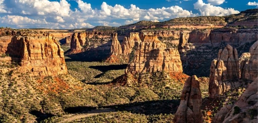 A sweeping view of rugged, reddish rock formations and valleys under a blue sky with clouds.