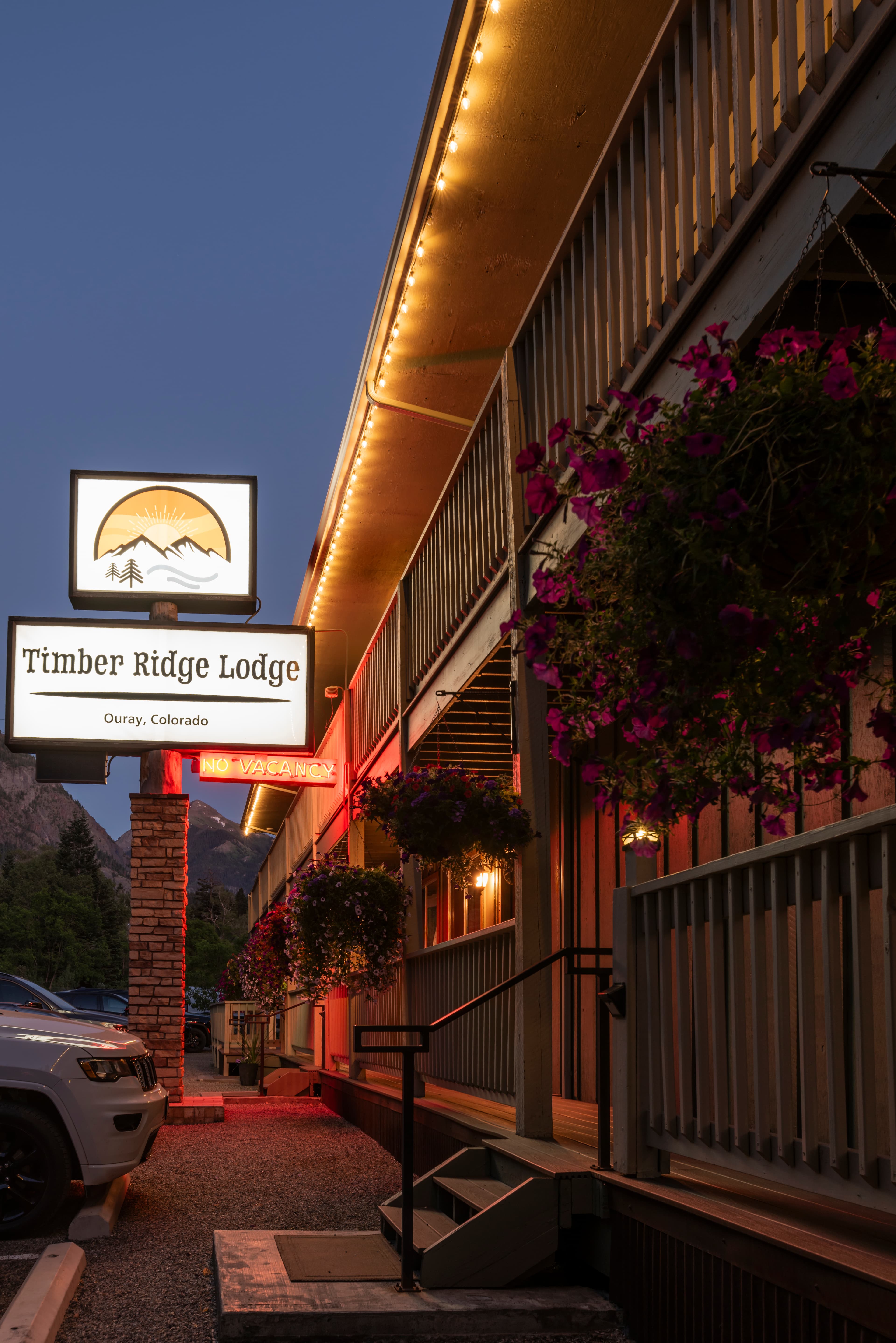 Timber Ridge Lodge sign illuminated at dusk in Ouray, Colorado, with hanging flower baskets nearby.