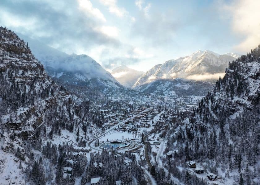 Snow-covered mountains surround a picturesque valley town under a cloudy sky.