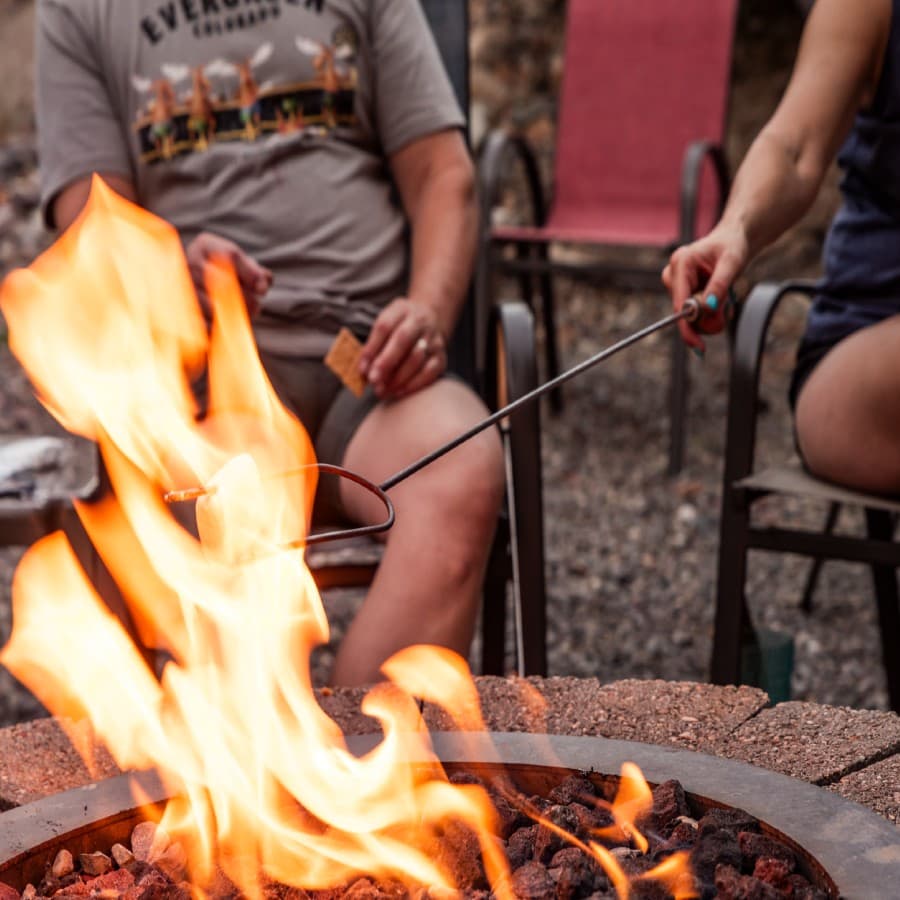 A person roasting a marshmallow over a campfire while sitting in a chair.