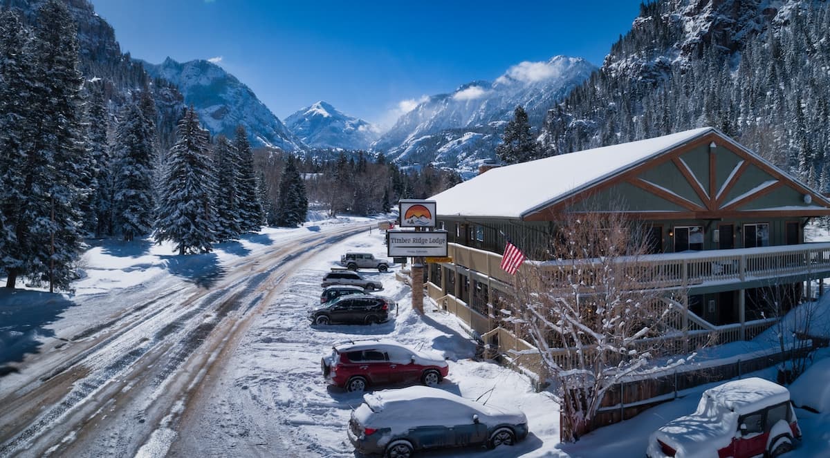 Snow-covered lodge surrounded by mountains and pine trees.