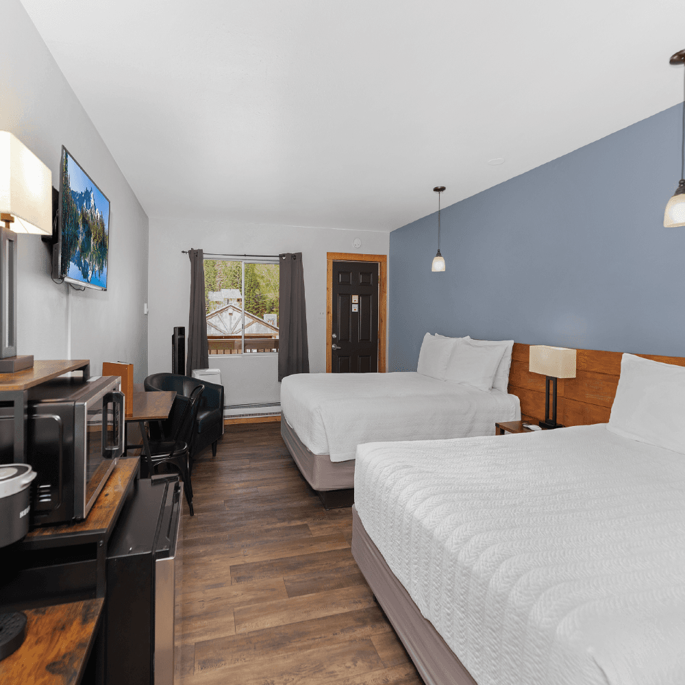 A cozy hotel room featuring two beds, a desk, a microwave, and a window with a view.