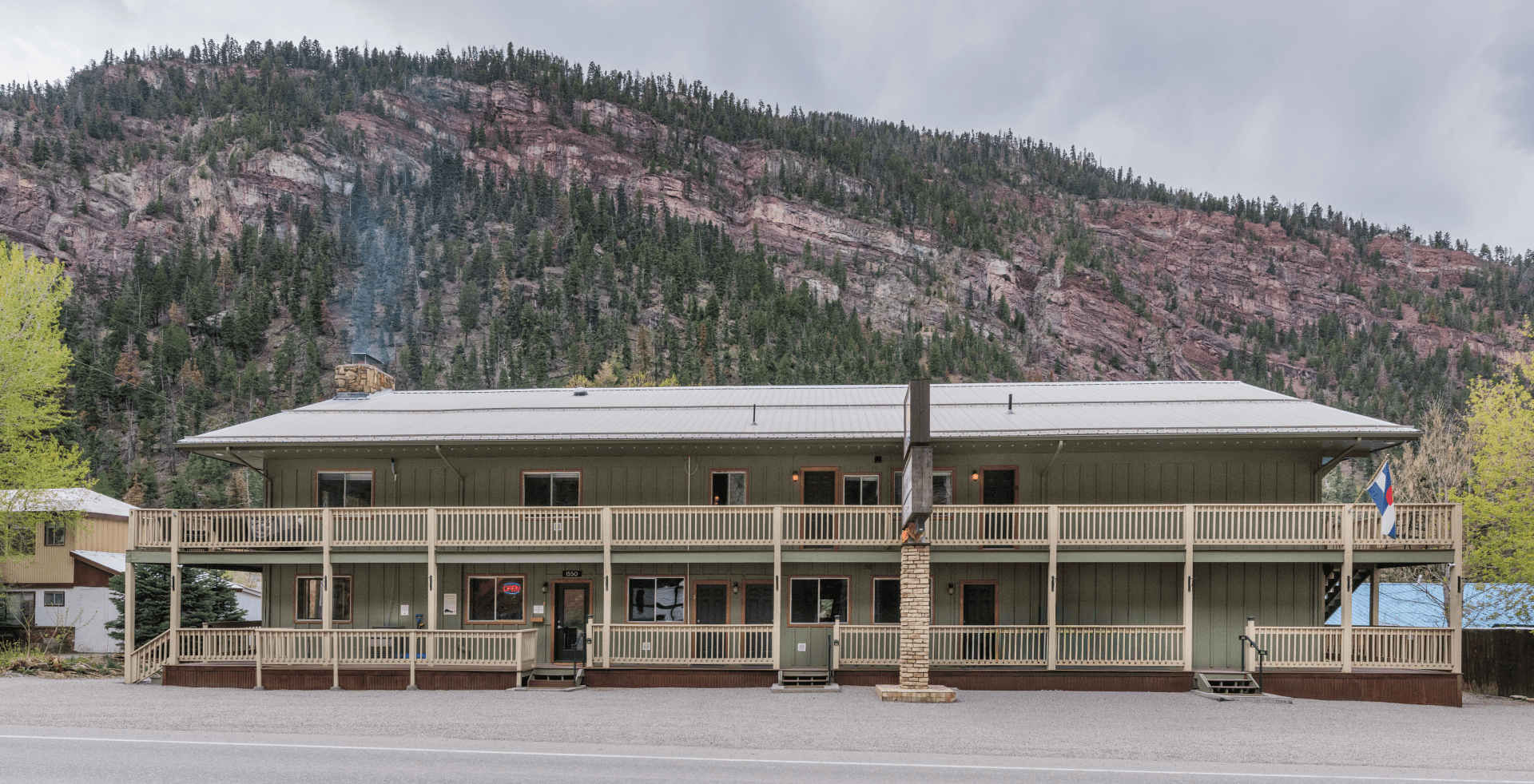 A two-story building with a covered porch nestled against a mountainous backdrop.