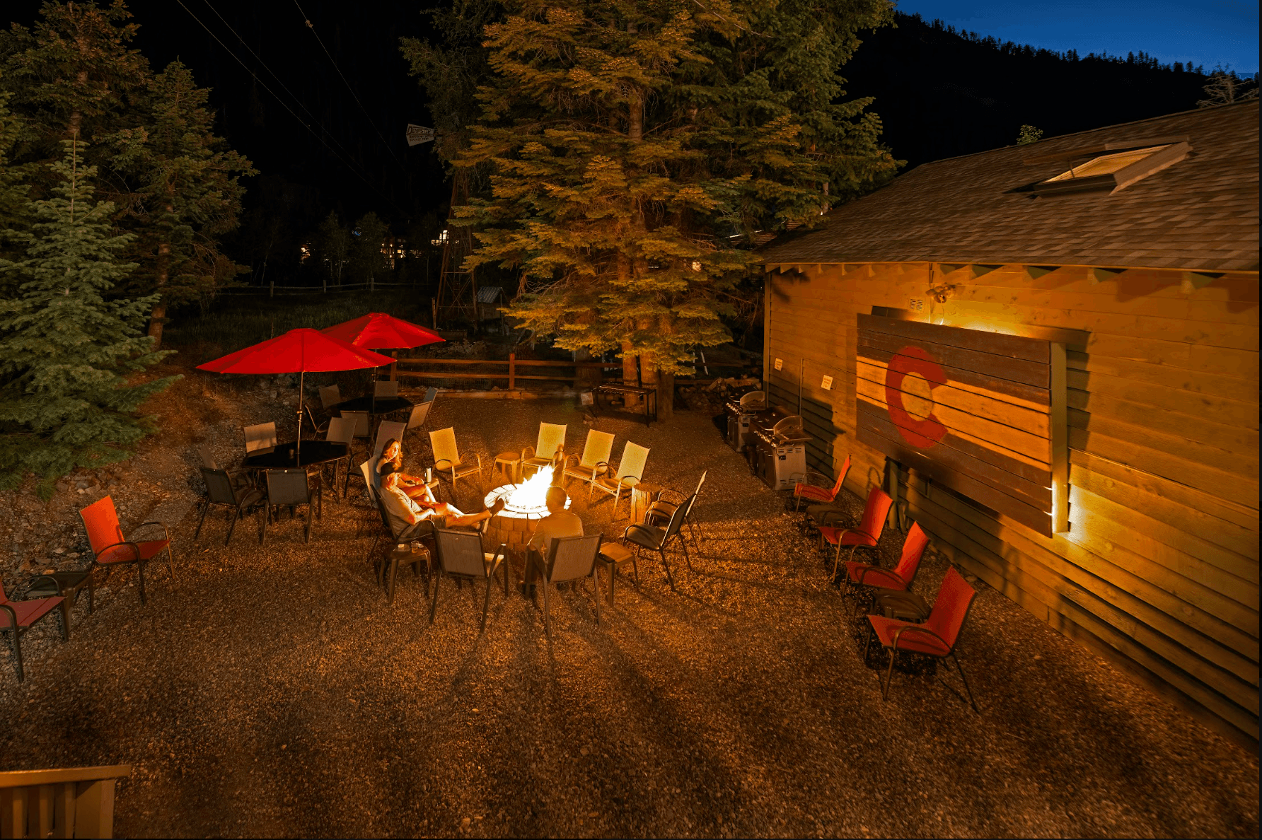 A cozy outdoor gathering area with a fire pit surrounded by chairs, under a night sky.