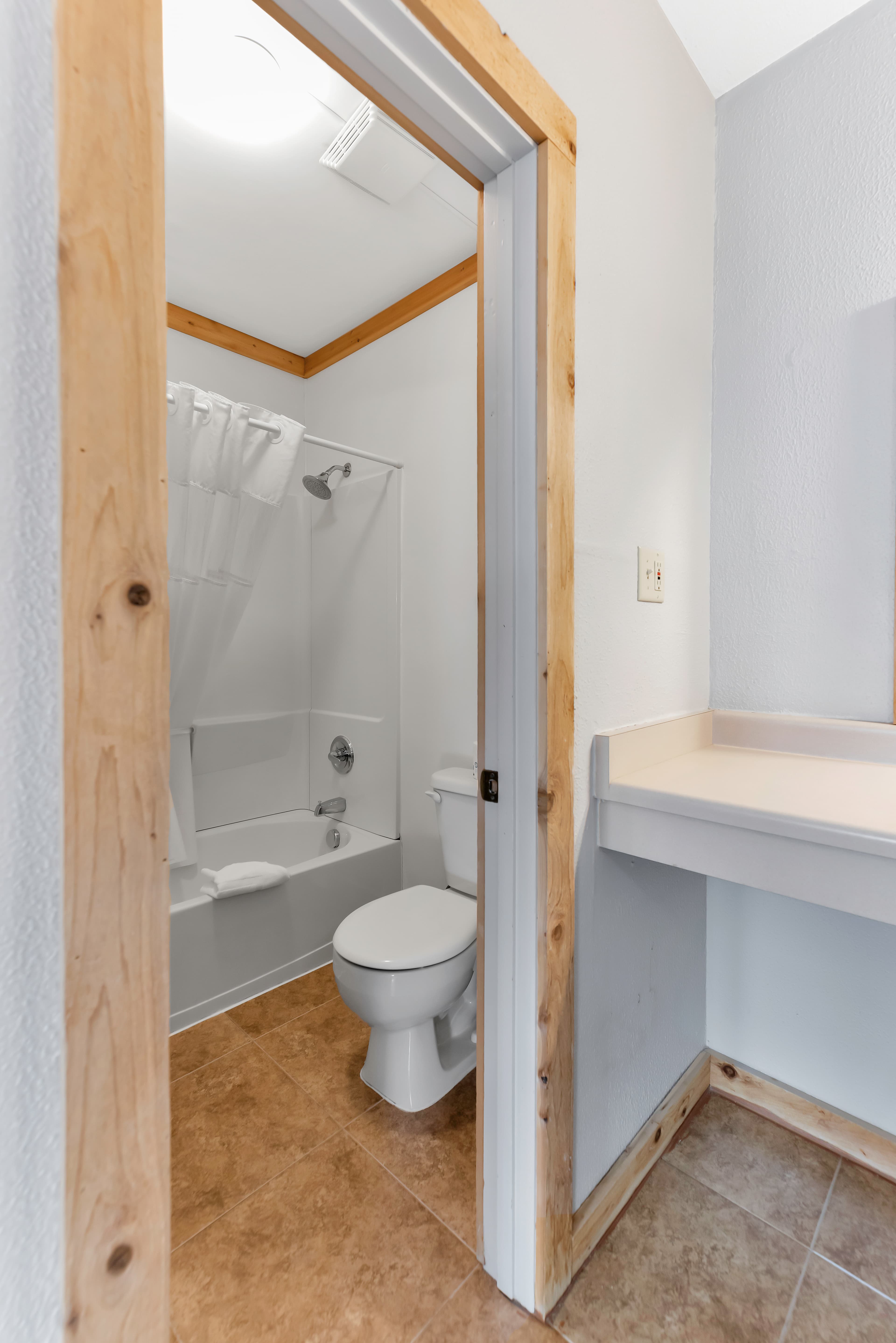 A clean, updated bathroom in the Queen Room showing a white bathtub-shower combo and toilet. The space is finished with warm tan floor tiles and natural wood door trim, reflecting the rustic lodge aesthetic of this Ouray, Colorado accommodation.