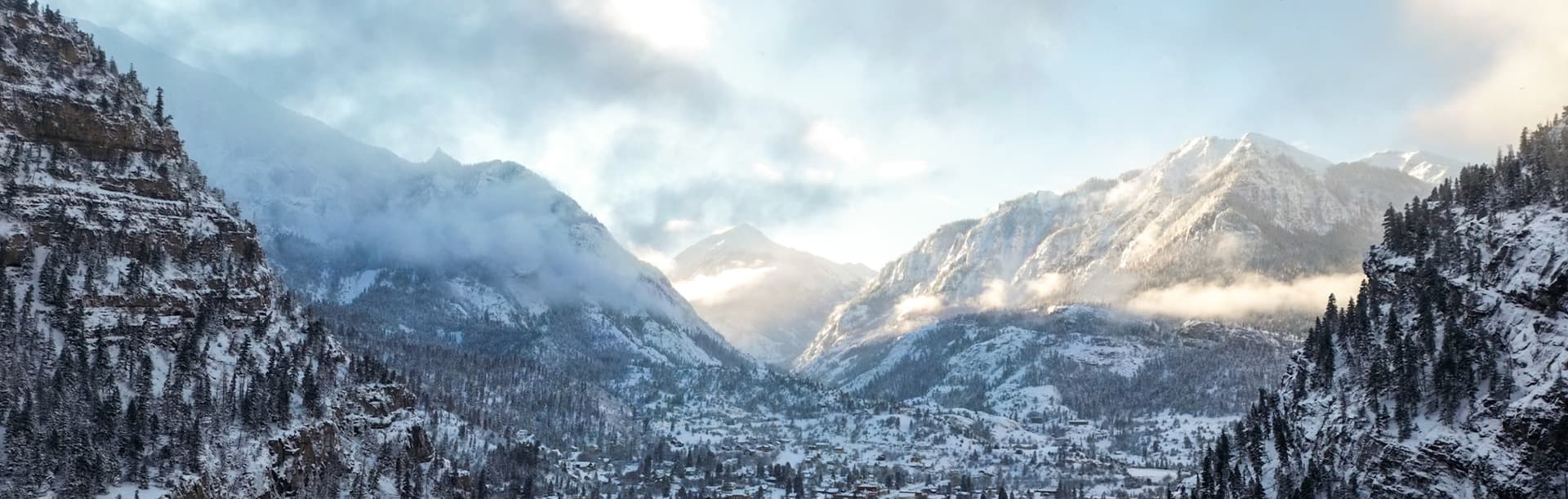 Snow-covered mountains surrounded by a valley under a cloudy sky.