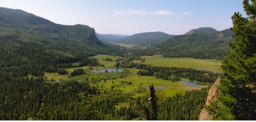 A panoramic view of a lush green valley surrounded by mountains and lakes under a clear blue sky.