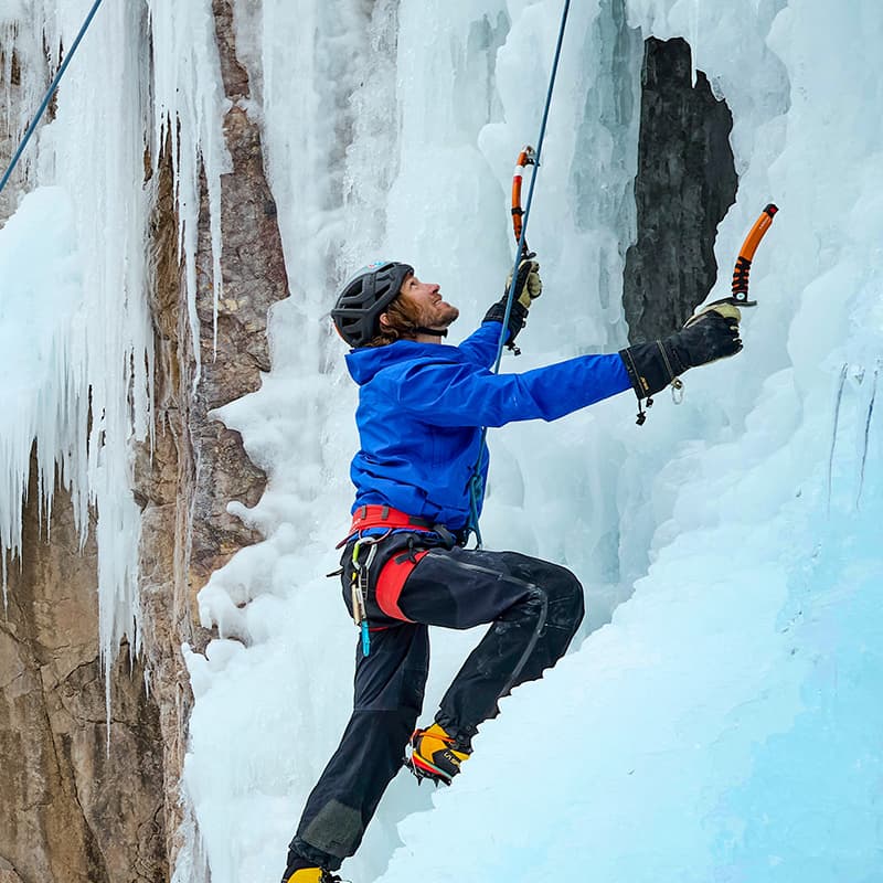 A climber ascends an ice wall using ice axes and climbing gear.