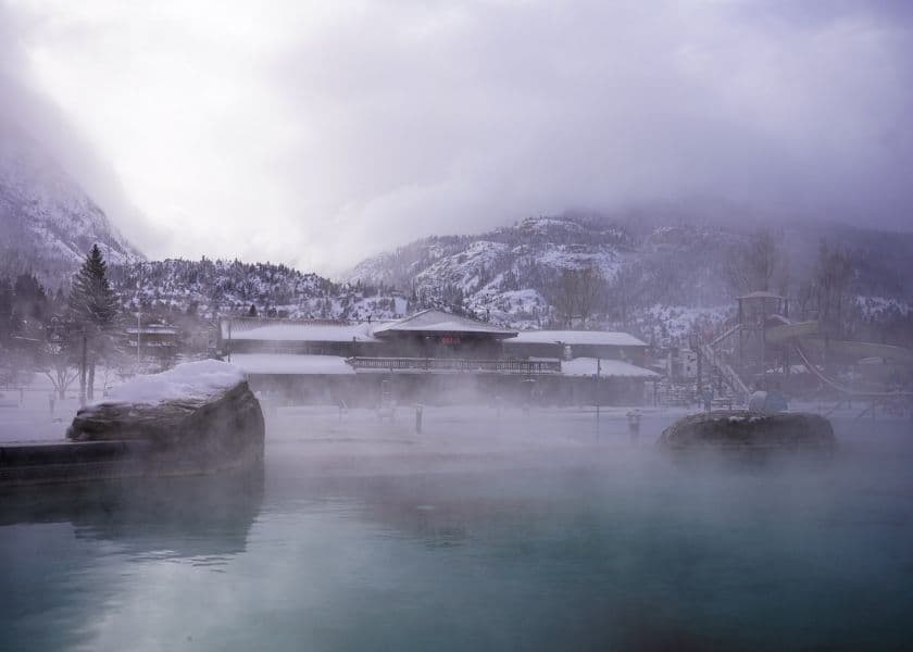 Steaming outdoor hot springs pool in Ouray, Co, with snowy mountains in the background.
